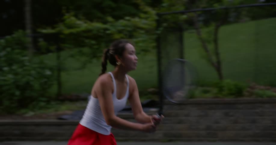Teenage girl hitting a tennis ball to her opponent on the other side of the court