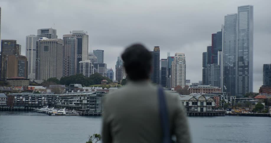 Person adjusts a bag on their shoulder while looking across a river at the city