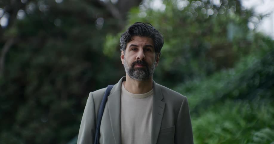 An older man wearing a suit jacket standing in front of trees
