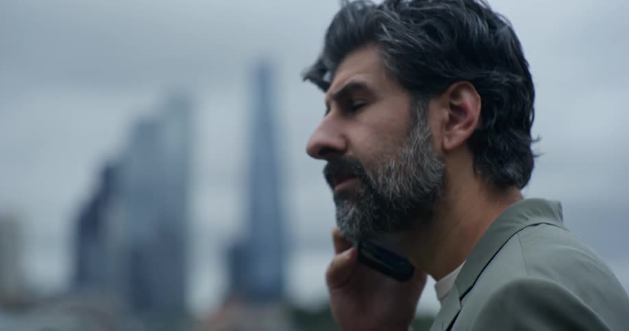 A bearded man talking on a smartphone with a city skyline in the background