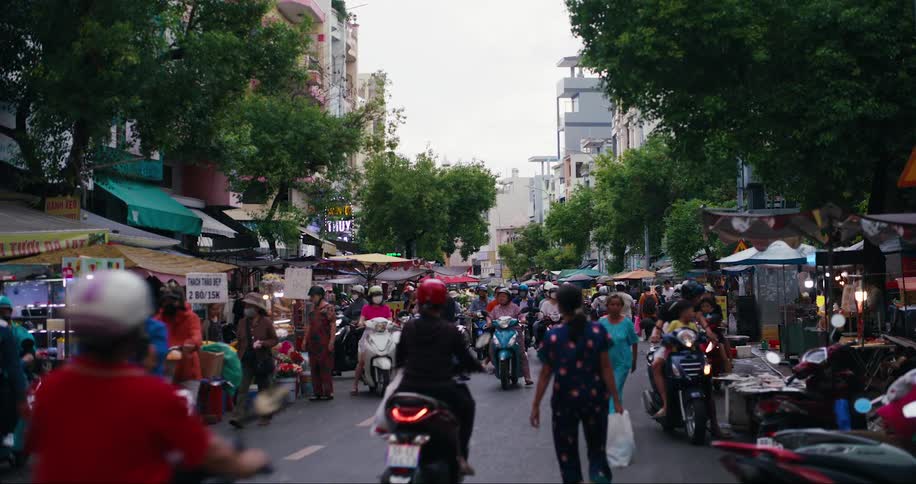 Large crowds of asians walk or drive vehicles through an outdoor marketplace in a city