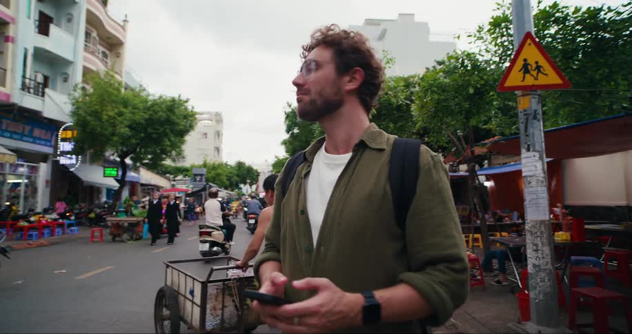 Portrait of a male tourist with a cell phone in his hands observing a busy street with small markets around