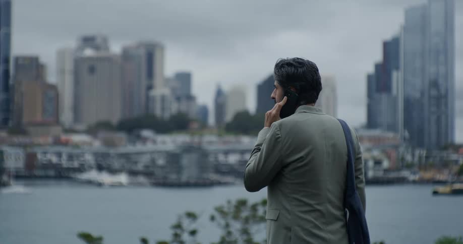 Man in a suit using a smartphone in front of a sea canal with buildings of a metropolis in the background