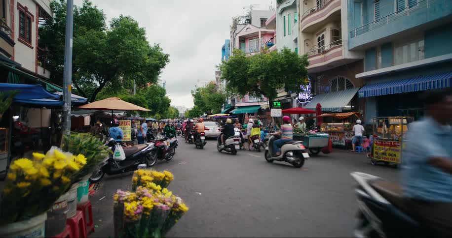 People walk and ride motorcycles up and down an asian city street