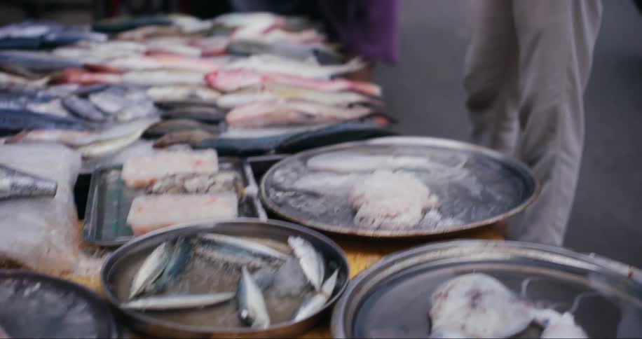 Man watching fish and squid being sold in a grocery store next to a busy street