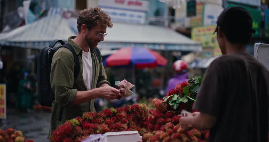 Man handing a banknote to a fruit vendor in a grocery store in the middle of the street