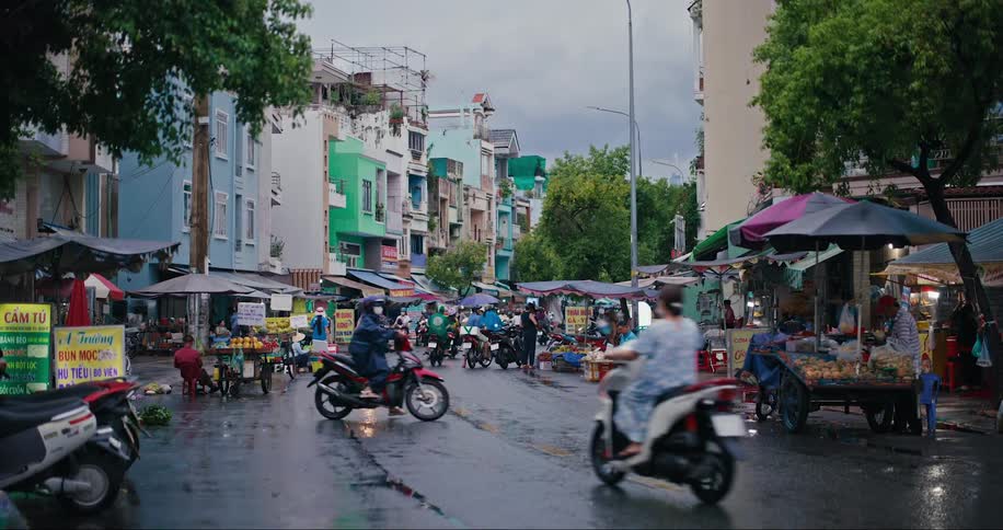 Street busy with pedestrians and motorcyclists and with small markets in the surrounding area