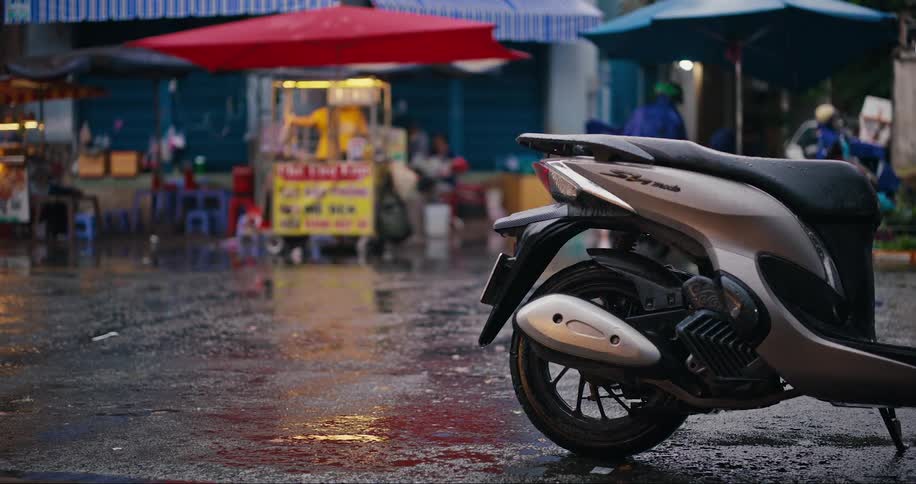 Motorcycles passing through a narrow and wet street with shops around
