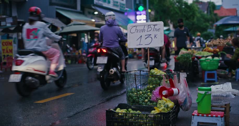A nonstop stream of people riding motorcycles past a marketplace in a city
