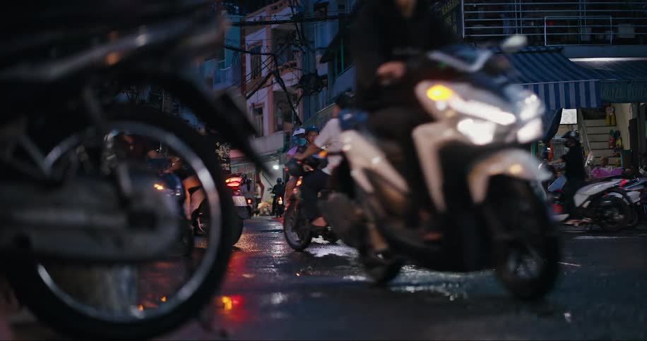 Lots of people ride motorcycles down a crowded street at night in an asian city