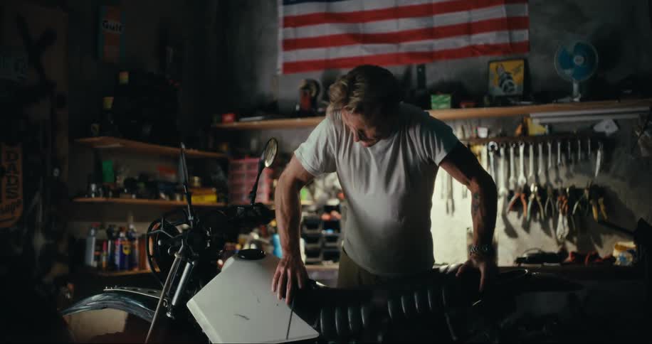 Man struggling to put his cell phone on a black bench on a motorcycle inside a workshop