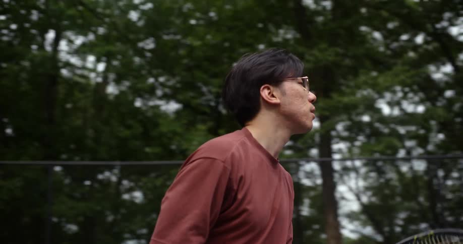 An asian races around a court while playing tennis with an opponent