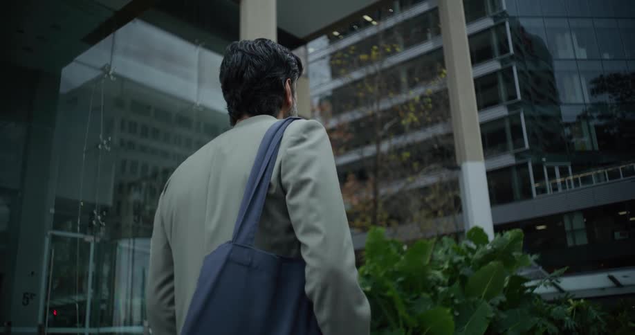A man carrying a shoulder bag walks on the city looking at the buildings