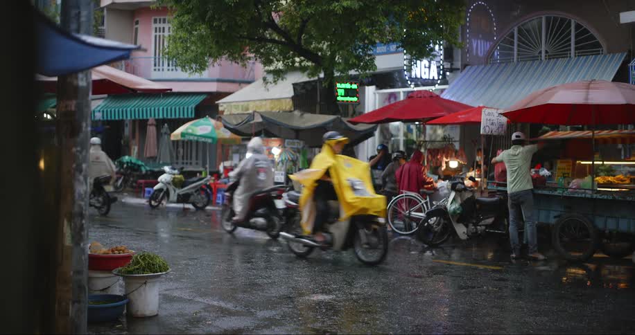Motorcycles passing by on a street on a rainy day with stalls selling food around