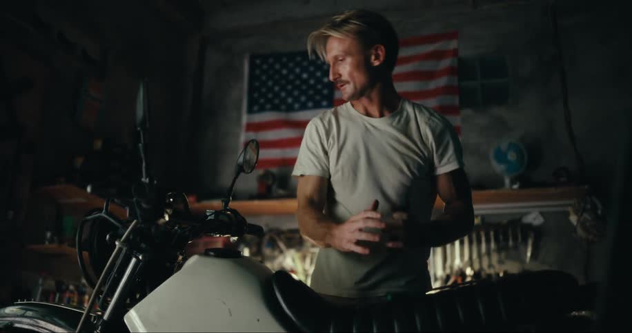 Man doing mechanical work on a motorcycle inside of a dark garage