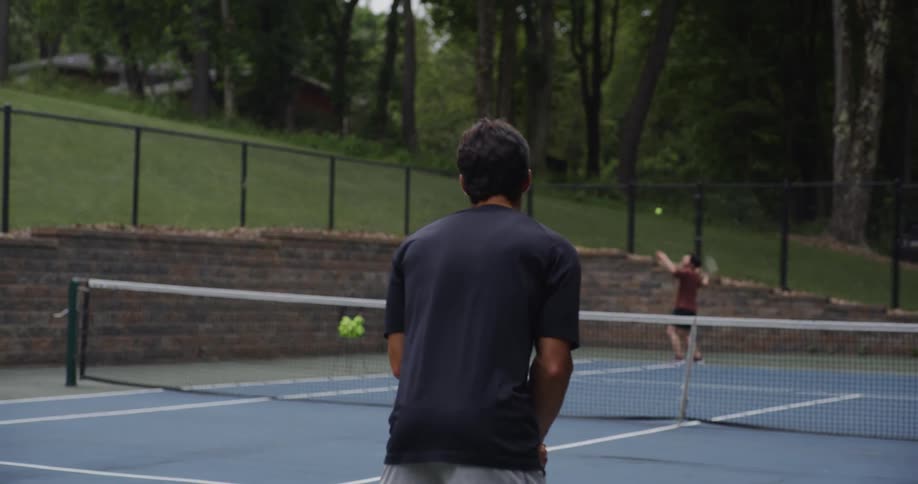 Two young men play tennis on an outdoor court