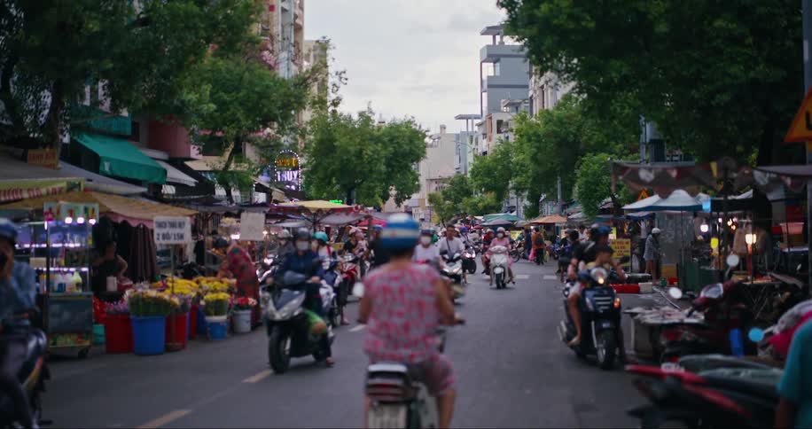 Customers shop at road side shops on a street busy with motorcycles and other two wheeled traffic
