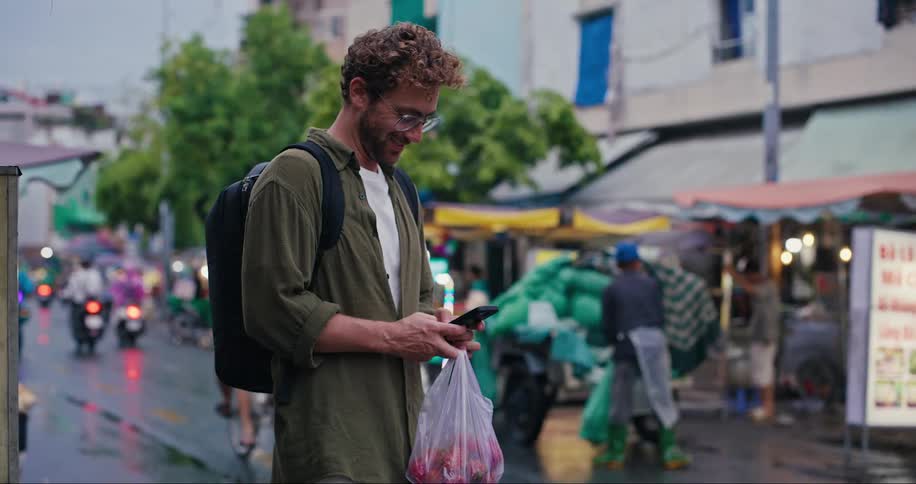 Man using his cell phone while standing on a busy street with street markets and vehicle traffic