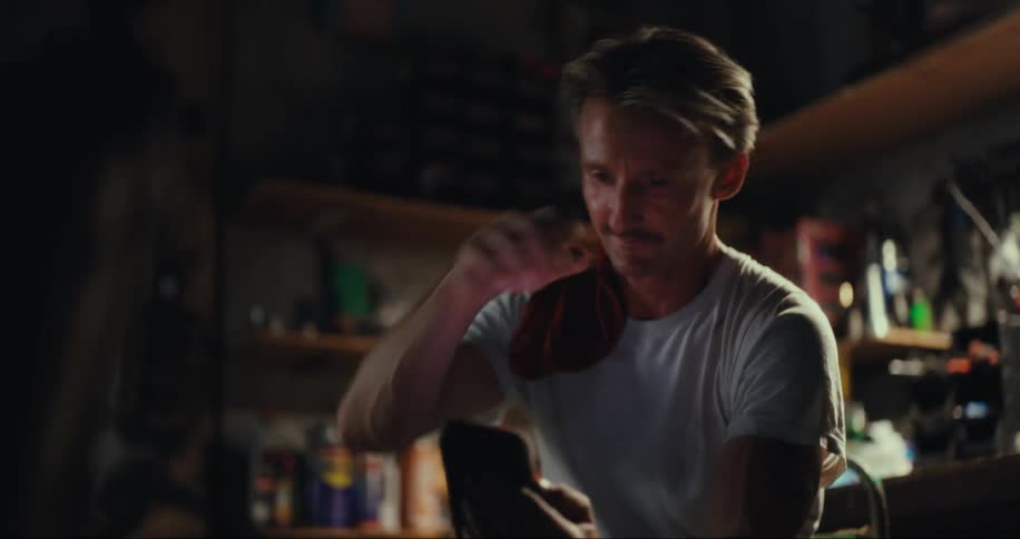 Man sitting in a garage with tools using his cell phone and rubbing his forehead