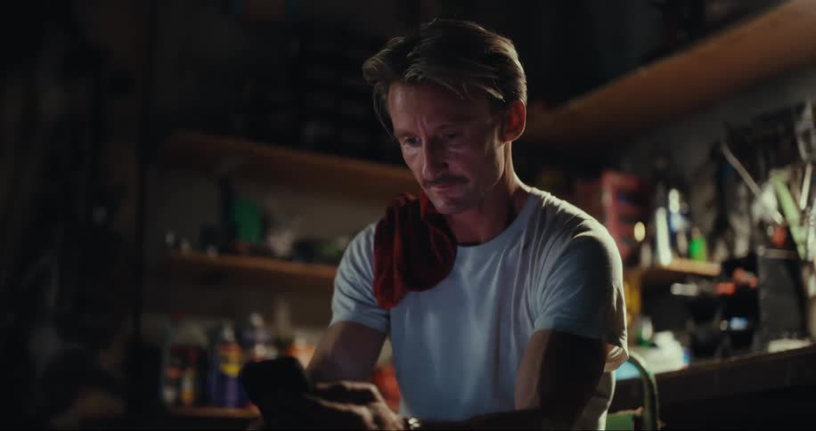 A man sitting in his garage workshop checks his phone thoughtfully