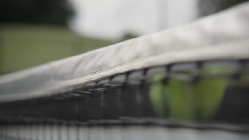 A closeup view of a tennis net as a tennis balls hits it