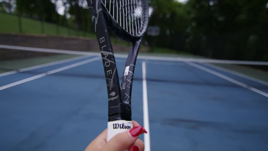 A woman tapes the handle of her tennis racquet while standing on an outdoor court