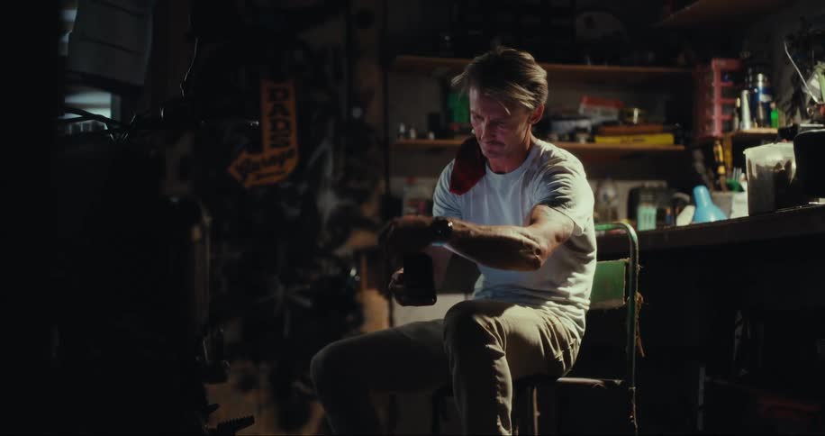 Blond man sitting in a garage on a chair typing on a smartphone