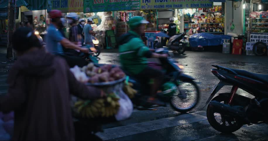 A bustling city street teems with motorcycles and street food vendors