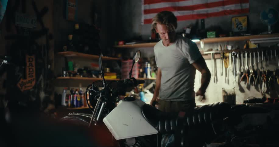 A man in a garage tests a motorcycles headlight then lifts its seat to look for something under it