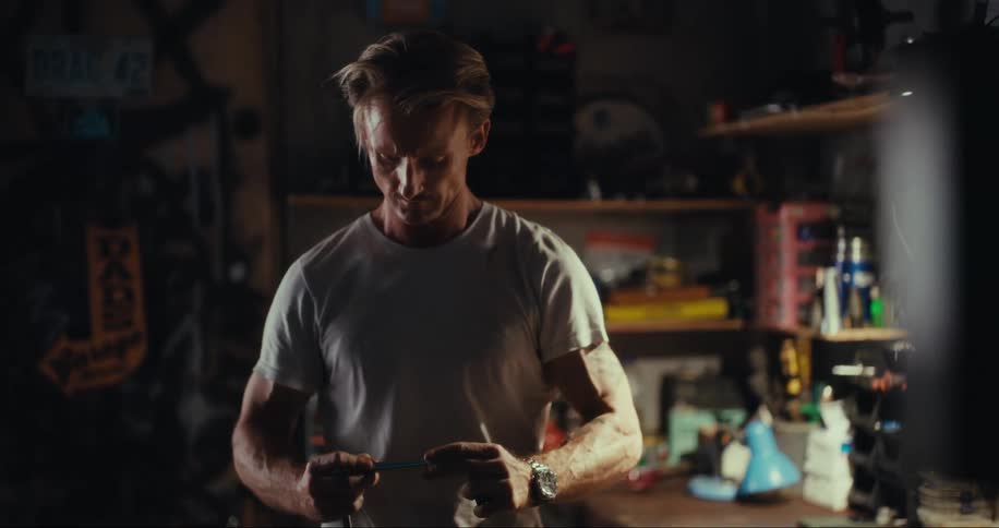 Man in a garage picking up a tool and wiping it down