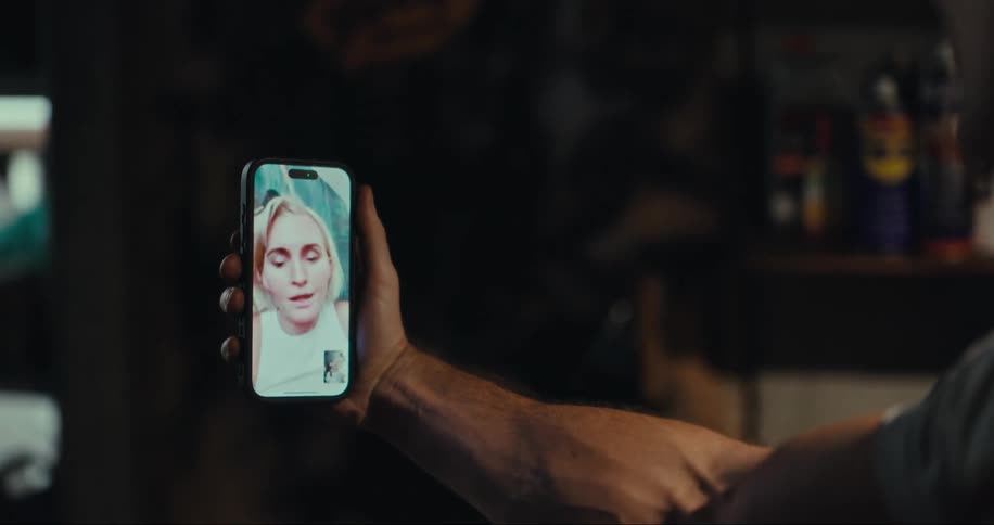 A man holds a smartphone and listens and watches a woman streaming herself on it