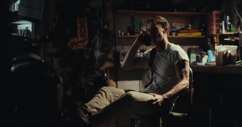 A man sits in a chair in a garage and talks on a smartphone