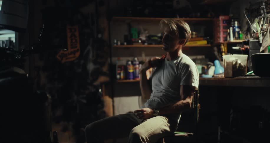 A man sits down in a garage and grabs a bottle of water