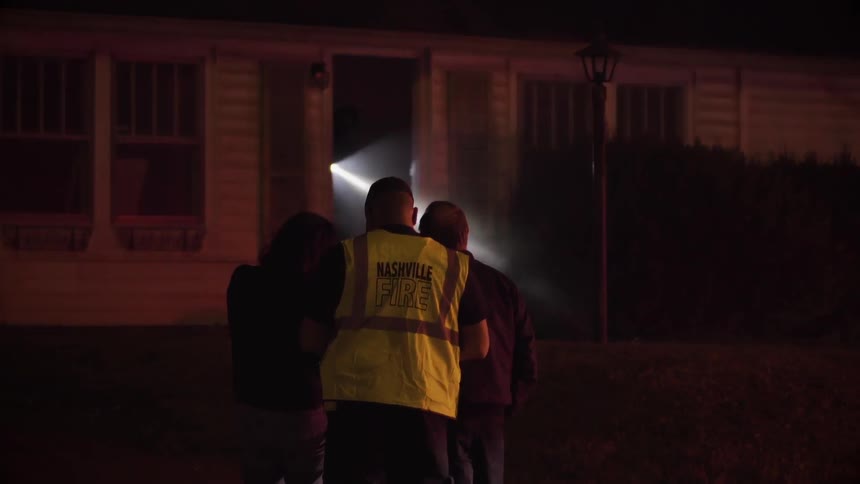 A fireman consoles a couple outside their house at night