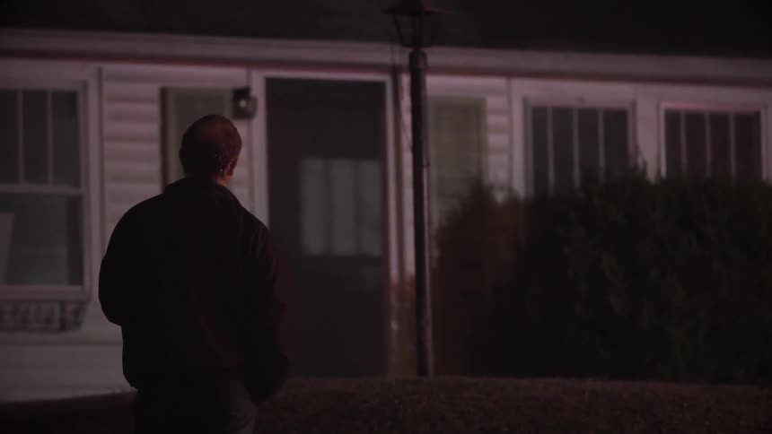 A man is standing in front of a home with emergency lights flashing on it