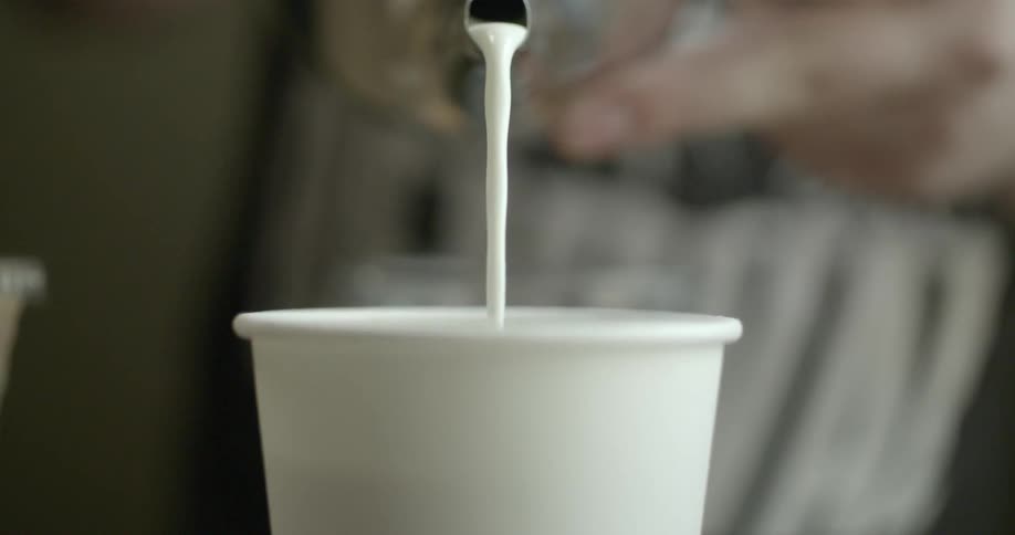 A barista pours milk into a coffee cup