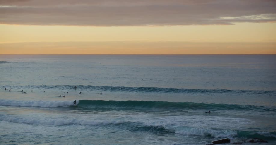 A beach with some waves breaking near the shore and some people in the water and there are some surfers surfing the waves