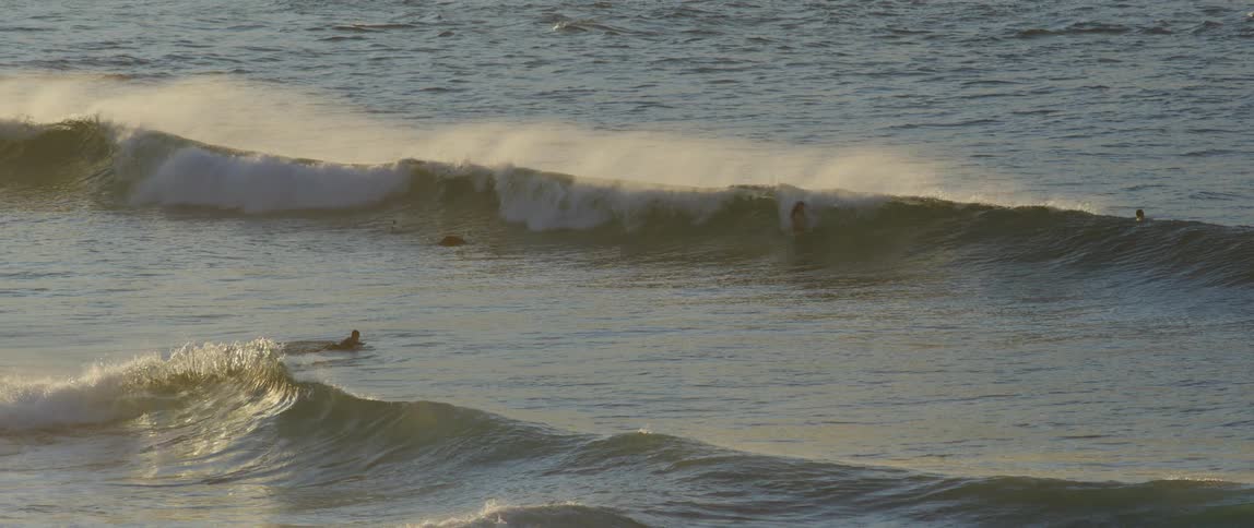 Surfers on a beach with waves in a morning