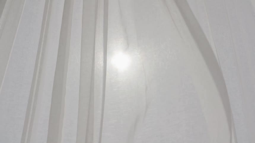 Sunlight shines through a curtain on a bright blue sky
