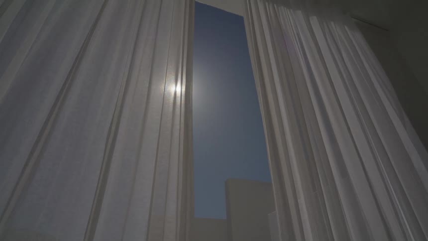 View of the sun in a clear sky from the window with a white curtain