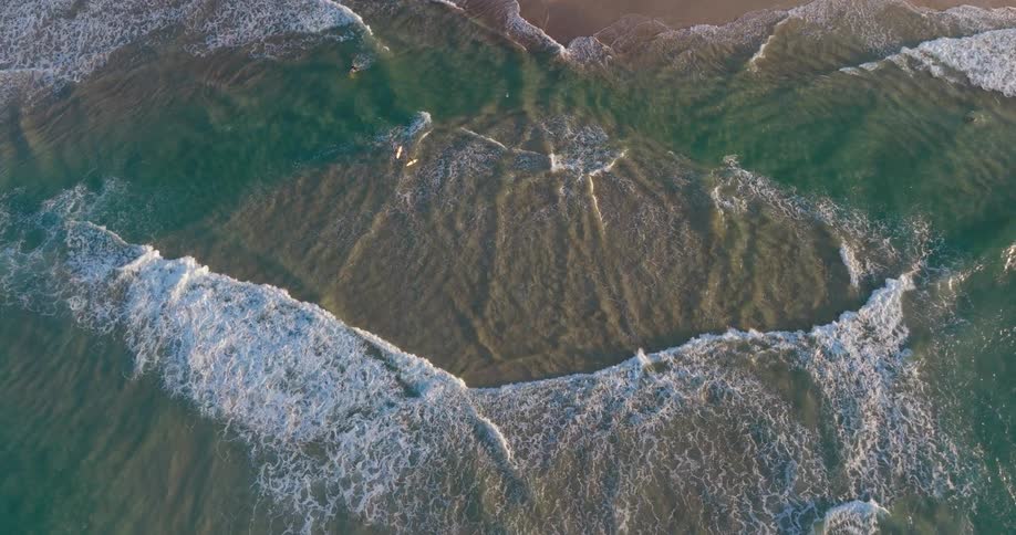 Aerial view of waves on a crystal clear beach reaching a strip of sand