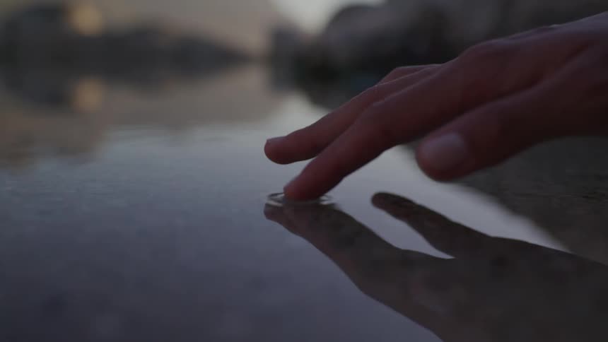 An individuals finger touches the water causing a tiny ripple