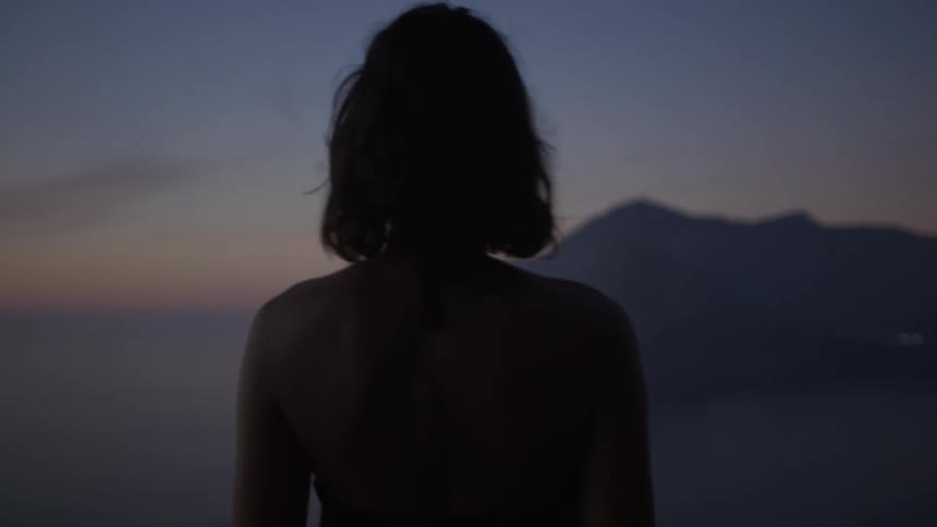 Back of a beautiful woman looking at an island during sunset
