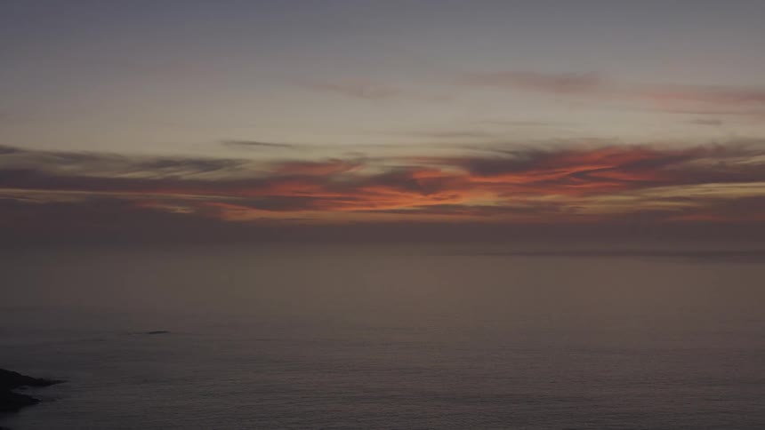 An ocean that stretches to the horizon in a calm landscape and in the sky the clouds that are partially illuminated by the sunlight in the morning