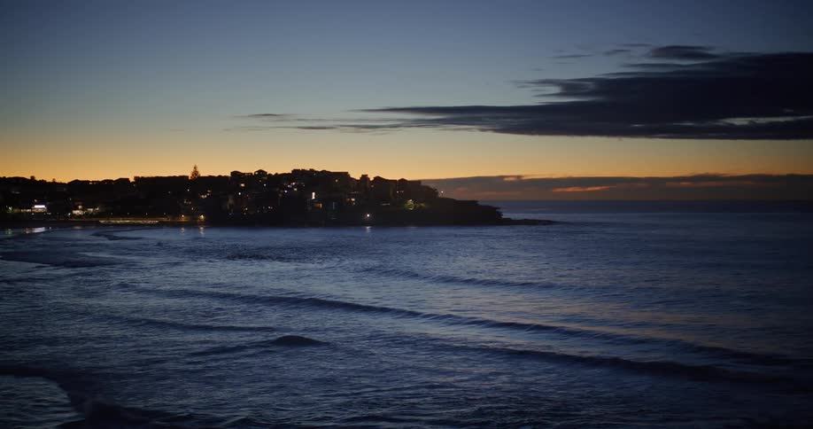 Landscape of a beach with calm waves and a city on the coast in the background at dusk