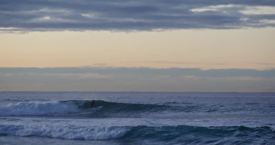 Several people surfing on a big wave on a cloudy evening at dusk