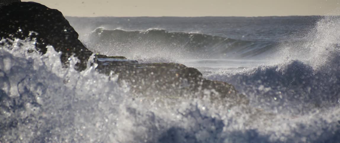 Big waves crash against the dark stone shore spraying water into the air