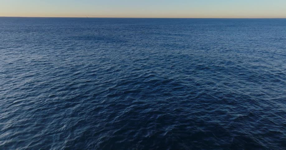 Aerial landscape of a vast ocean with an orange sky on the horizon