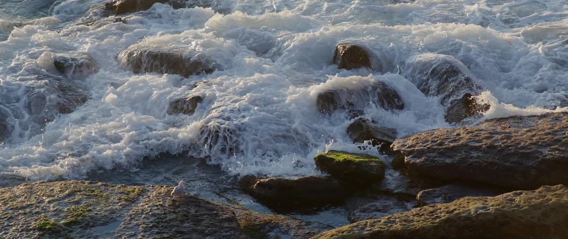 Ocean waves crash over large rocks in slow motion