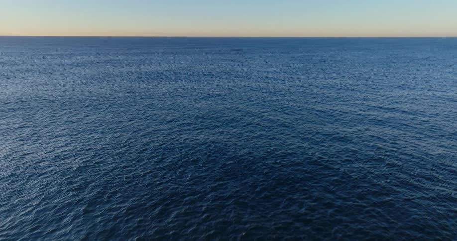 Wind waves flow across blue ocean waters as red tints the horizon